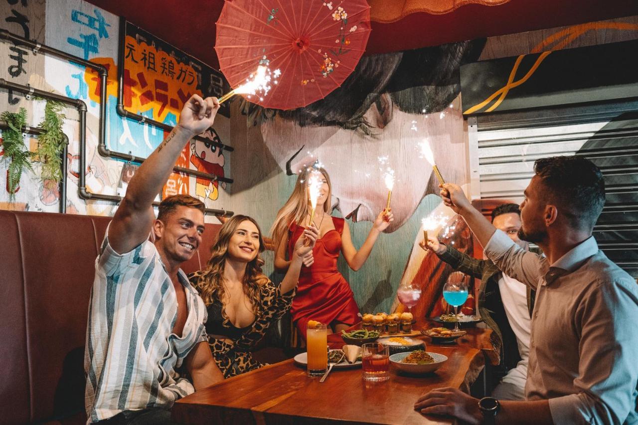 Five Jumeirah Village Dubai Buitenkant foto The photo depicts a lively gathering at a dining table where several people are celebrating. There are four individuals: two men and two women. One of the women is wearing a red dress, while the other is dressed in a patterned outfit. They are holdin