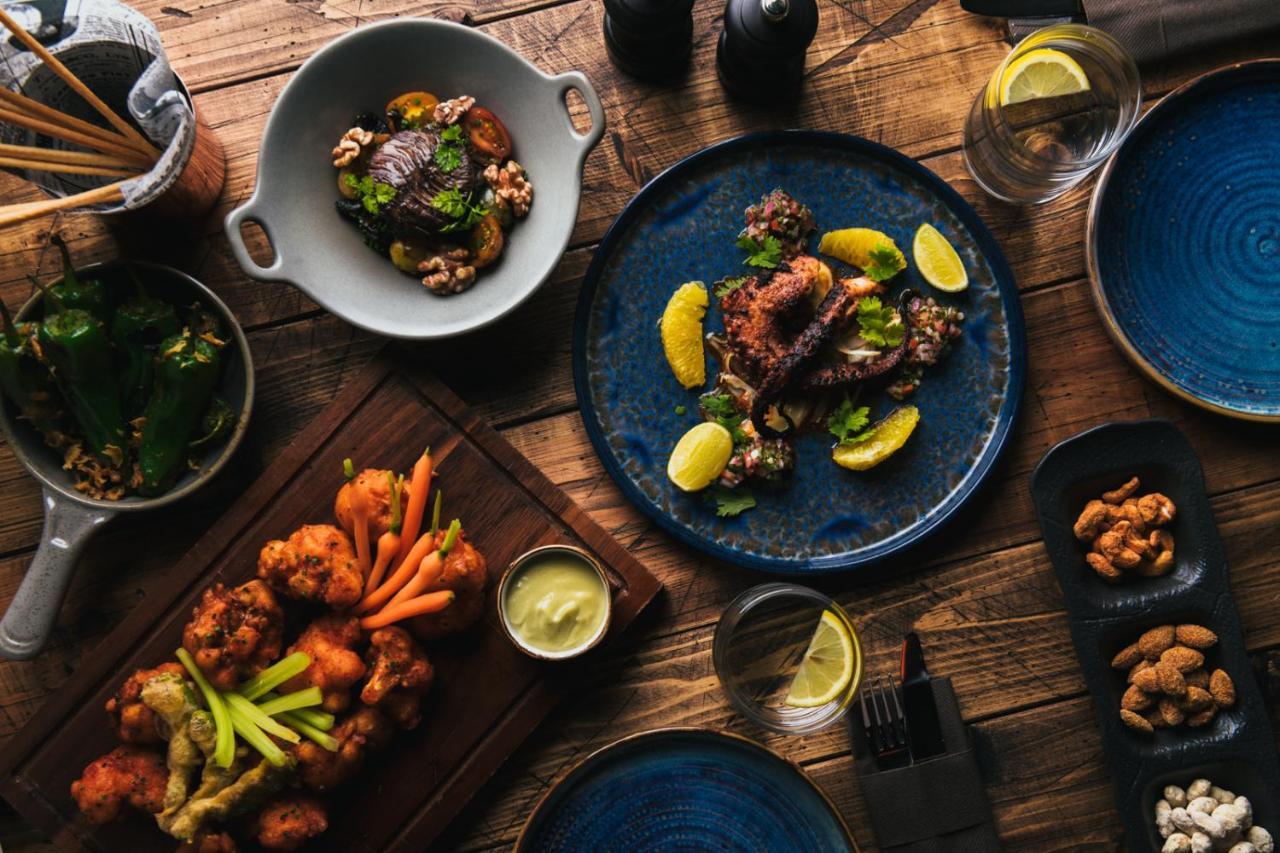 Five Jumeirah Village Dubai Buitenkant foto The photo displays a beautifully arranged spread of various dishes on a wooden table. 

1. In the center, there's a blue plate featuring a main dish garnished with lemon slices and fresh herbs.
2. To the left, another dish includes fried pieces, like