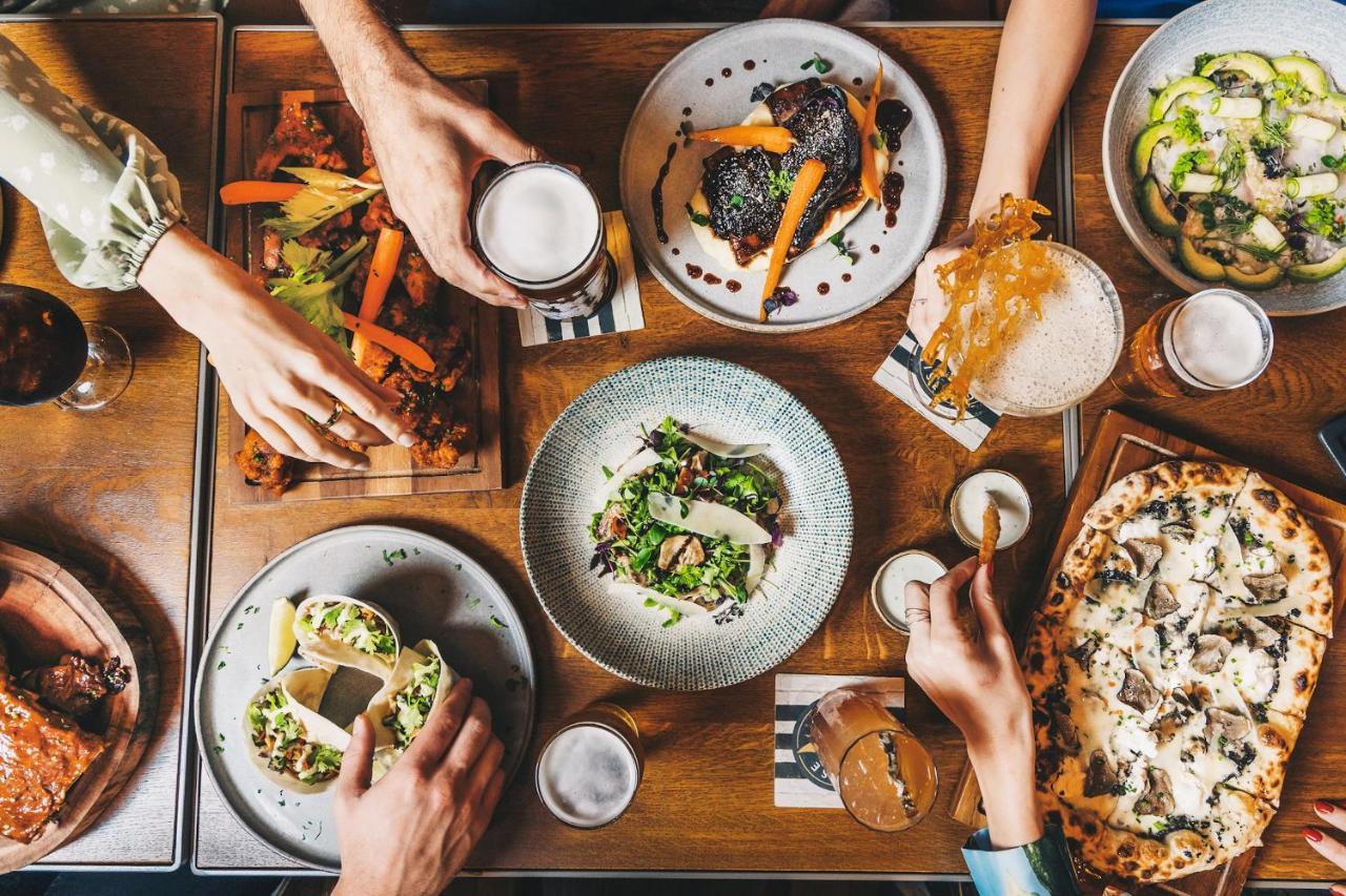 Five Jumeirah Village Dubai Buitenkant foto The photo displays a table filled with a variety of delicious food and drinks. There are several dishes, including a colorful salad in a round bowl, tacos, and what appears to be a pizza. On the side, there are also wooden platters with grilled veget