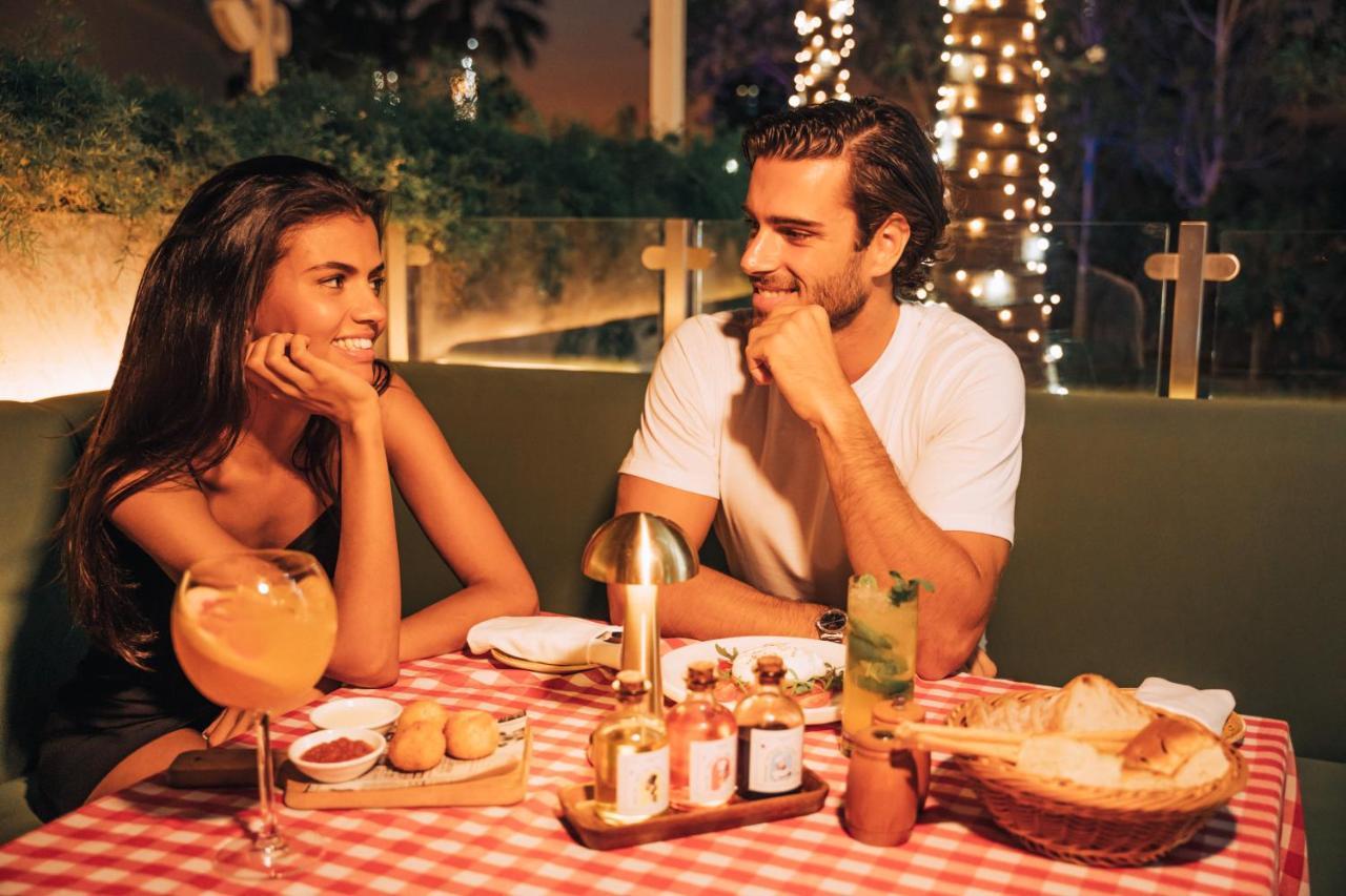 Five Jumeirah Village Dubai Buitenkant foto The photo shows a romantic dining scene featuring a couple at a table. The setting is illuminated with soft lights, creating a warm atmosphere. The table is adorned with a red and white checkered tablecloth, and various dishes are presented, includin