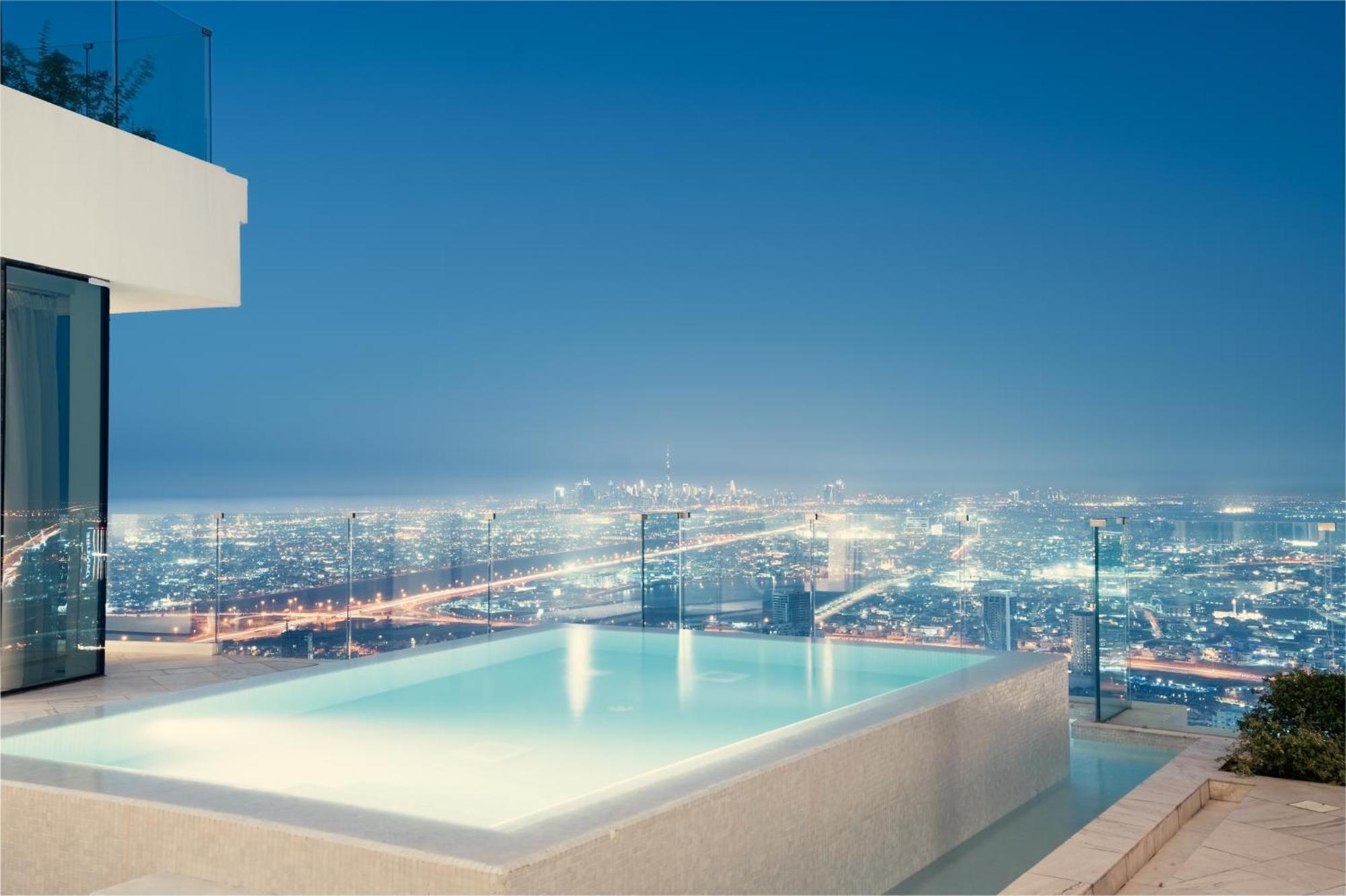 Five Jumeirah Village Dubai Buitenkant foto The photo showcases a luxurious infinity pool situated on an elevated terrace, overlooking a sprawling cityscape at night. The pool's water has a serene glow, reflecting the city lights below, which shimmer and create a vibrant backdrop. The architec