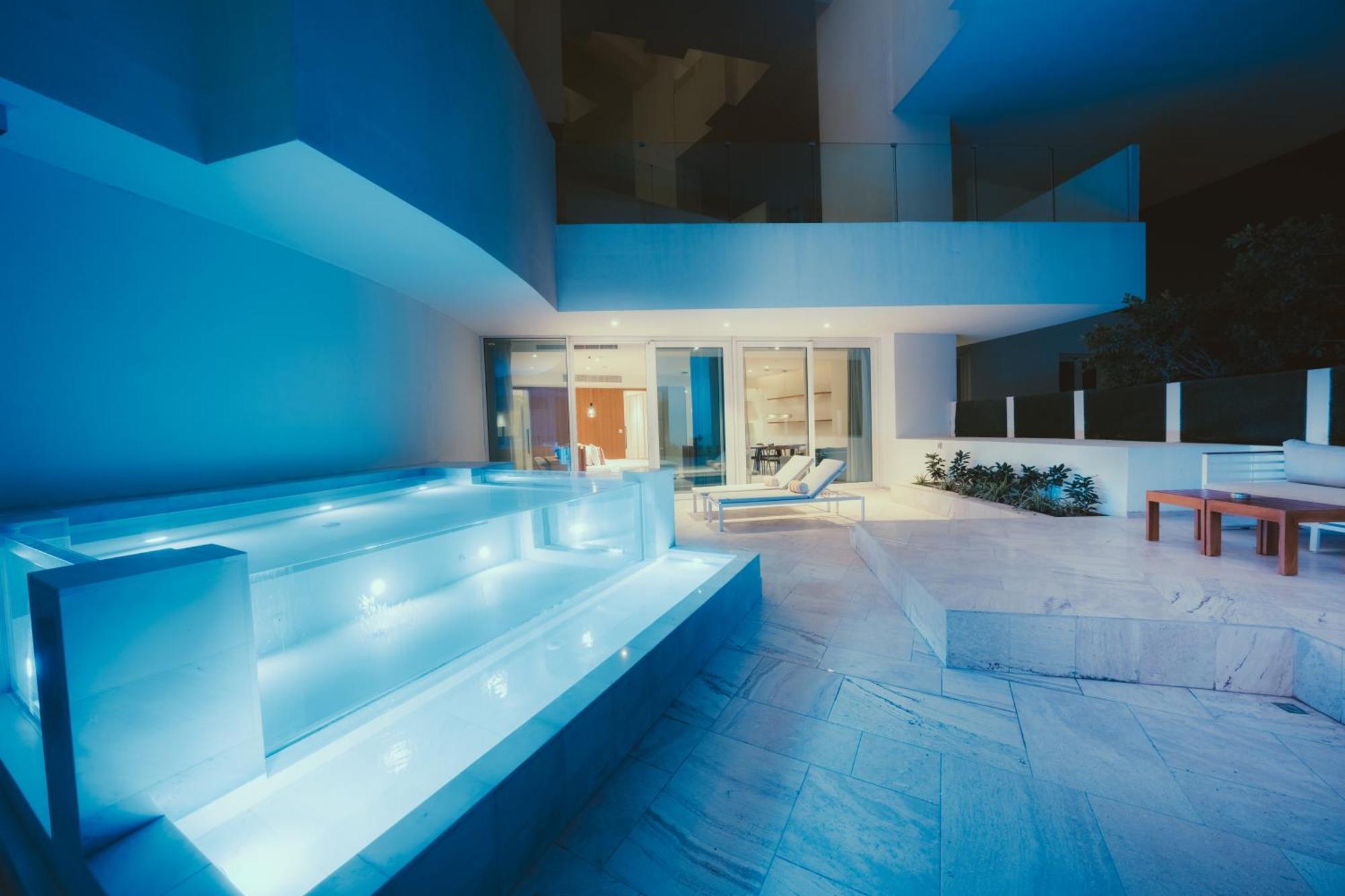 Five Jumeirah Village Dubai Buitenkant foto The photo shows a modern outdoor area, likely part of a contemporary home. It features a stylish, illuminated staircase leading down to a pool or water feature, with soft blue lighting that creates a serene atmosphere. In the background, large glass 