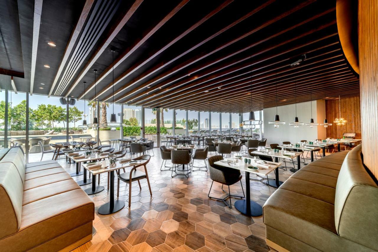 Five Jumeirah Village Dubai Buitenkant foto The photo shows the interior of a modern restaurant. It features a spacious layout with a combination of wooden and tiled flooring, characterized by hexagonal tiles. The ceiling has a modern design with wooden beams that add a sophisticated touch. Th